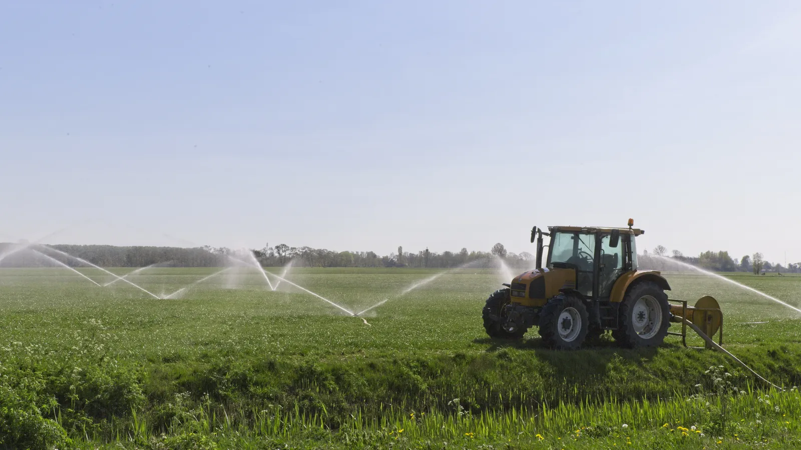 Trattore che irriga un campo agricolo con impianto a pioggia